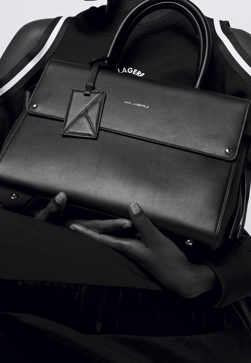 Black leather handbag with a structured design, smooth texture, top handles, and a small embossed brand logo on the front.