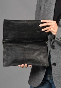 Clutch de piel negra con una textura suave, que cuenta con un compartimento con cremallera y un diseño abierto, sostenido por una persona que lleva una chaqueta gris.