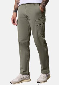 Pantalones cargo en verde oliva con un corte recto, que cuentan con bolsillos laterales y una tela suave y ligera. Combinados con zapatillas beige.