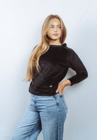 Musta, pehmeä kangastoppi pitkällä hihalla, rento istuvuus ja pyöreä kaula-aukko; yhdistetty vaaleansinisiin korkeavyötäröisiin farkkuihin.