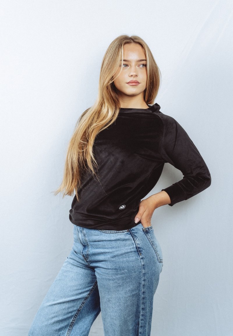 Musta, pehmeä kangastoppi pitkällä hihalla, rento istuvuus ja pyöreä kaula-aukko; yhdistetty vaaleansinisiin korkeavyötäröisiin farkkuihin.