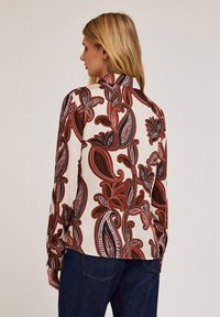 Bluză cu mâneci lungi, de culoare crem, cu un model paisley roșu și negru, având guler și manșete cu nasturi. Textură de țesătură netedă.
