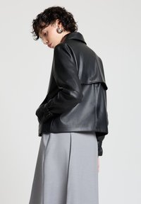 Schwarze Lederjacke mit lockerem Schnitt, ausgestattet mit einem breiten Kragen und einem detaillierten Schulterdesign, kombiniert mit einem grauen Rock.