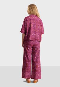 Conjunto de dos piezas con un patrón ikat en rosa y púrpura, que incluye una blusa de manga corta y pantalones de pierna ancha. Tela suave con un ajuste holgado.