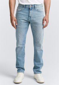Lichtblauwe denim jeans met een rechte pasvorm, vijf zakken en een iets verouderd effect. Gepaard met witte sneakers.