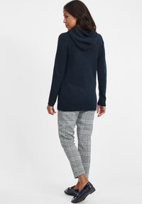 Mörkblå stickad cardigan med huva, långa ärmar; kombinerad med rutiga byxor i blått, svart och vitt. Svarta loafers fulländar outfiten.