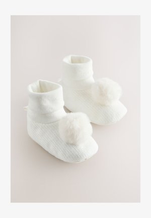 Bele pletene copatke z zložljivo manšetko in mehkimi umetnimi krznenimi cofki spredaj. Teksturirana površina z zaobljenim dizajnom prstov.