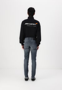 Must maikana McLareni logoga tagaosal, koos sobivate hallide teksade ja mustade tossudega, vaade tagant valge tausta vastu.