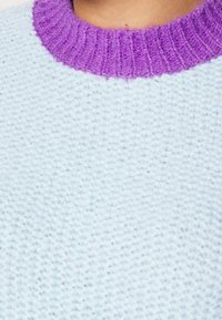 Pull bleu clair en tricot avec un col violet côtelé. Texture douce avec un motif de tissage lâche.