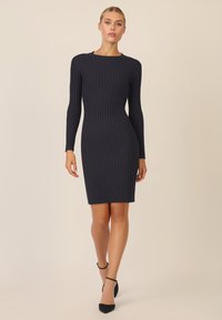 Rippiertes navy-blaues Kleid mit langen Ärmeln, schmaler Passform, rundem Ausschnitt, knielangem Schnitt, kombiniert mit schwarzen spitzen Absatzschuhen und Knöchelriemen.