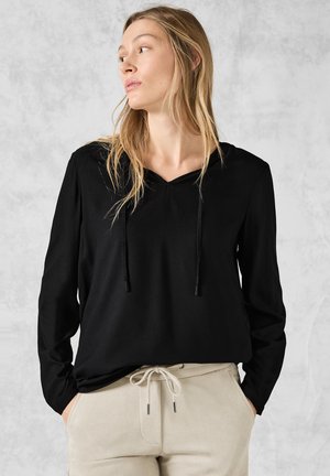 Zwarte lange mouw hoodie met een V-hals en trekkoord. Gemaakt van zachte stof, gecombineerd met beige broek.