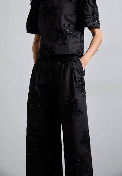 Juodas dviejų dalių komplektas, kuriame yra trumpas viršus ir platėjančios kelnės. Abu drabužiai papuošti tekstūriniu gėlių karoliukų raštu. Švelni medžiaga.