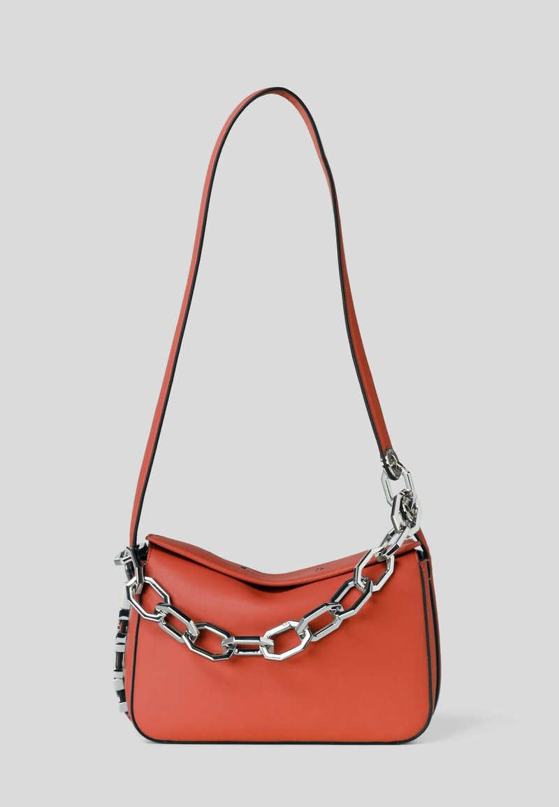 Rode leren schoudertas met lange schouderband en grote zilveren geometrische kettingdetail aan de voorkant, tegen een lichtgrijze achtergrond.