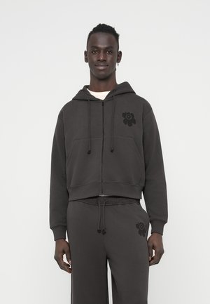 Κοντή σκοτεινή γκρι φούτερ με κουκούλα και μπροστινές τσέπες. Διαθέτει μαύρο λουλουδένιο σχέδιο στο αριστερό στήθος. Μαλακό, υφασμάτινο ύφασμα με υφή.