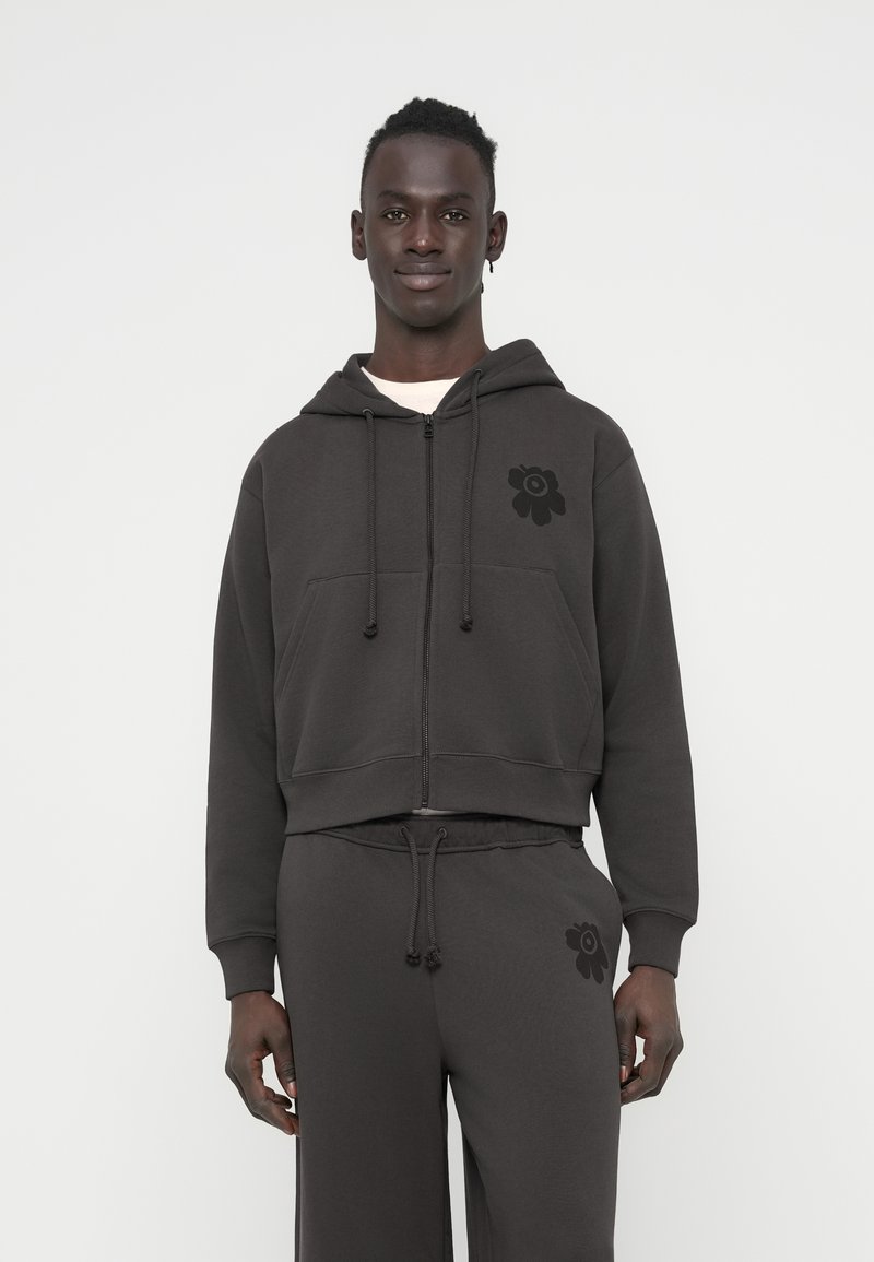 Κοντή σκοτεινή γκρι φούτερ με κουκούλα και μπροστινές τσέπες. Διαθέτει μαύρο λουλουδένιο σχέδιο στο αριστερό στήθος. Μαλακό, υφασμάτινο ύφασμα με υφή.