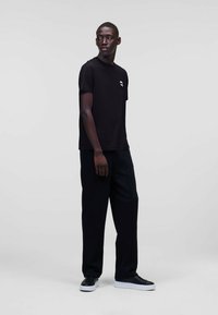 T-shirt nera in cotone con scollatura rotonda, maniche corte e piccolo grafico bianco sul petto, abbinata a pantaloni neri larghi e sneakers.