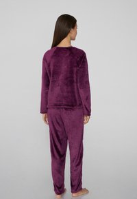 Conjunto de pijama de terciopelo púrpura con mangas largas y pantalones. La textura suave, el ajuste relajado y el minimalismo en los detalles de las costuras son visibles desde la vista trasera.