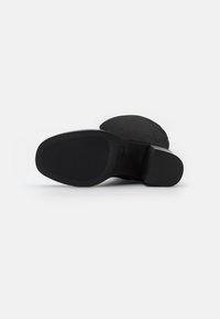 Bottine noire à tige lisse, semelle en caoutchouc texturée et bout arrondi. Présente des détails minimalistes et une finition mate subtile.