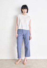 White short-sleeve crop top, light blue wide-leg jeans, and light tan mesh slip-on shoes. Model stands against a plain background.
