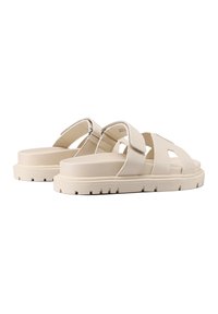 Sandali platform beige con cinturini incrociati, realizzati in materiale sintetico. Presentano una suola spessa e rigata con una texture liscia e dettagli metallici.