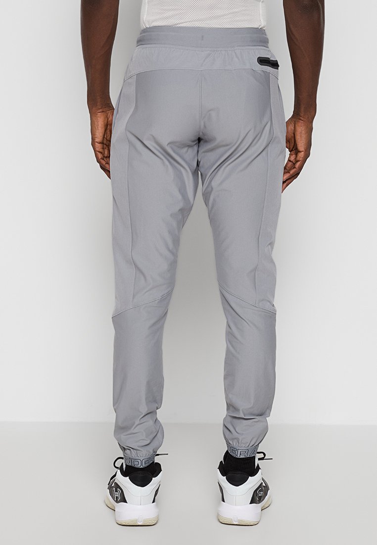 Pantalons de sport gris avec un design fuselé, taille élastique et poches latérales zippées. Le tissu semble léger et durable, avec des accents côtelés.