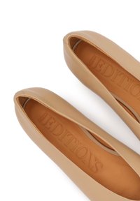 Chaussures plates en cuir nude élégantes avec une finition lisse, un design à bout ouvert arrondi, et une texture intérieure subtile présentant "EDITIONS" embossé dans le cuir.