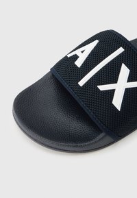 Ναυτικό σανδάλι slide με υφή από καουτσούκ στην επιφάνεια για το πάτημα και υφασμάτινο λουρί με έντονα λευκά γράμματα. Λεία επιφάνεια και στρογγυλεμένο σχέδιο στη μύτη.