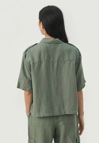 Khaki zelená, košeľa s krátkym rukávom a golierom, s ramennými epauletami. Mäkka tkanina s voľným strihom, kombinovaná s nohavicami v štýle cargo.
