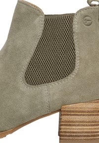 Zielone zamszowe botki za kostkę z teksturowanymi oliwkowymi panelami elastycznymi, przeszywanymi detalami oraz paskowym, przypominającym drewno obcasem.