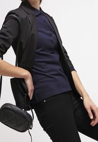 Polo shirt bleu marine avec un design à col et une patte de boutonnage à trois boutons, associé à un blazer noir et à un jean noir ajusté. Petit sac noir matelassé.