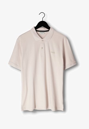 Licht beige polo-shirt met korte mouwen en kraag, met twee knopen, hangend aan een zwarte hanger, met klein Calvin Klein-logo op de borst.