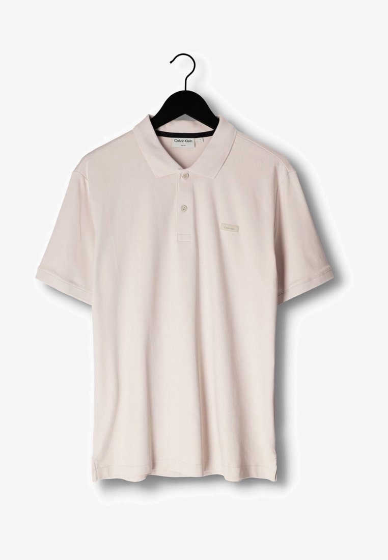 Ljusbeige kortärmad polotröja med krage och två knappar, hängande på svart klädhängare, med en liten Calvin Klein-logga på bröstet.