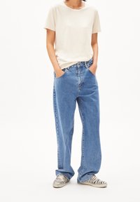 Helles beige Baumwoll-T-Shirt kombiniert mit locker sitzenden blauen Jeans. Die Jeans haben eine hohe Taille und ein klassisches Fünf-Taschen-Design.