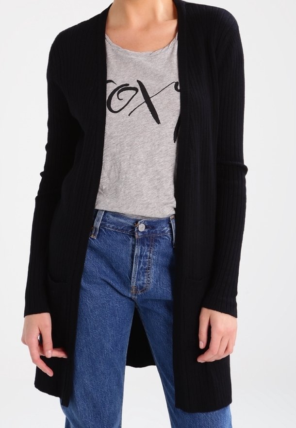 Schwarze gerippte Strickjacke mit offenem Vorderteil, langen Ärmeln und zwei Fronttaschen, getragen über einem grauen Grafik-T-Shirt und blauen hochgeschnittenen Jeans.