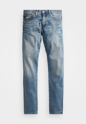 Niebieskie dżinsy denim o wąskim kroju, z pięcioma kieszeniami, zapięciem na guziki i wyblakłymi detalami prania na białym tle.