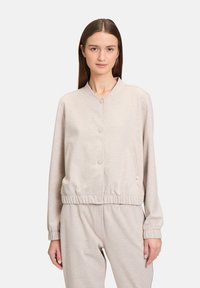 Jasno beżowa bluza z kapturem, miękki materiał, okrąg ły kołnierz, guziki z przodu, elastyczne mankiety i dół, kieszeń po bokach, luźny krój.