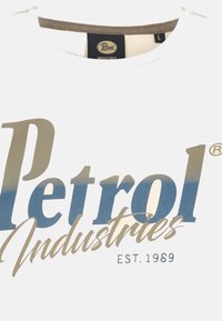 Hvid T-shirt med et stort blåt og gyldent "Petrol Industries" logo med teksten "EST. 1989" i mindre skrift. Rund hals design.
