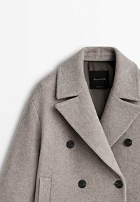 Manteau en laine gris clair à double boutonnage avec larges revers et boutons noirs, montrant la partie avant supérieure et la zone du col.