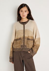 Ανοιχτό μπροστινό κάρντιγκαν σε μπεζ και καφέ αποχρώσεις. Διαθέτει δύο μπροστινές τσέπες, ριμπ τελείωμα και υφή πλέξης. Χαλαρή εφαρμογή με φαρδιές μανσέτες.