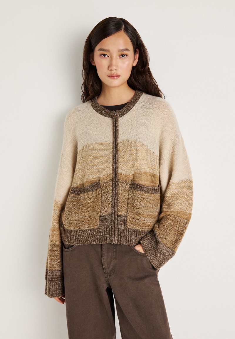 Ανοιχτό μπροστινό κάρντιγκαν σε μπεζ και καφέ αποχρώσεις. Διαθέτει δύο μπροστινές τσέπες, ριμπ τελείωμα και υφή πλέξης. Χαλαρή εφαρμογή με φαρδιές μανσέτες.