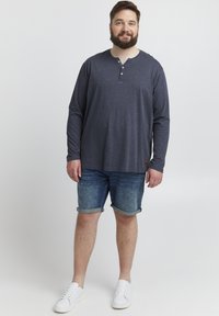 Hall värvi pika varrukaga henley särk koos kolme nööbiga, selga pandud rullitud denim lühikeste pükste ja valgete spordijalanõudega. Mõnus, pehme tekstuuriga riietus.