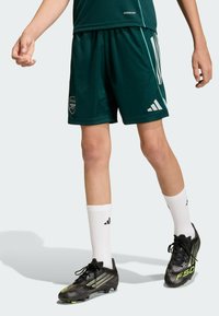 Pantalones cortos deportivos verdes con el logo del Arsenal, combinados con botas de fútbol negras con acentos verdes y calcetas blancas con logo negro.