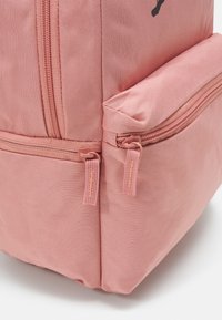 Zaino rosa chiaro con tessuto testurizzato, dotato di due tasche con zip sul davanti, ciascuna con cursori abbinati.