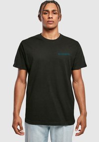 Zwarte katoenen t-shirt met korte mouwen. Teal "Iron Maiden" logo op de linkerborst. Klassieke pasvorm, stevige stof, minimalistische stijl.