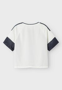 Kortermet hvit topp med marineblå detaljer på skuldrene og ermene. Laget av lett materiale med en teksturert overflate og rund hals.