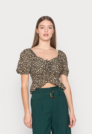 Top de flores preto, cropped, com mangas bufantes, detalhe franzido na frente e barra ondulada. Combinado com calças verdes de cintura alta e uma fivela circular.