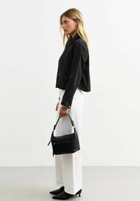 Chaqueta negra corta con botones, pantalones blancos de cintura alta y un bolso de piel negra con un bolsillo con cremallera y correa corta. Tacones puntiagudos negros.