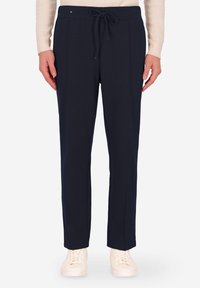 Pantaloni jogger blu navy realizzati in materiale morbido, con waistband regolabile con cordino, cuciture laterali e vestibilità rilassata, abbinati a sneakers bianche.