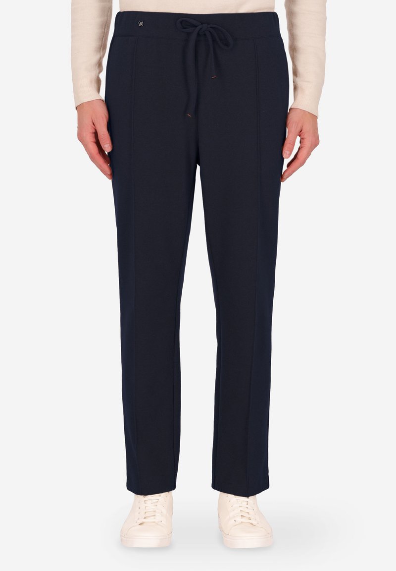 Pantaloni jogger blu navy realizzati in materiale morbido, con waistband regolabile con cordino, cuciture laterali e vestibilità rilassata, abbinati a sneakers bianche.