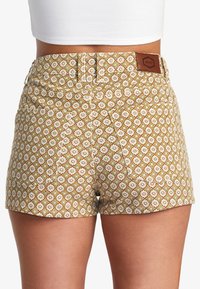 Musterhose in Braun mit einem floralen Design in Weiß und Grün. Mit Gesäßtaschen und einem Leder-Logo-Patch am Bund.